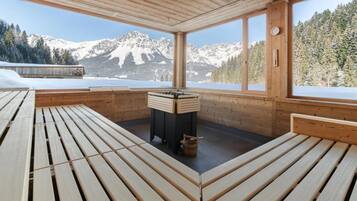 A wooden deck with benches, a fireplace, and a view of snow-covered mountains.