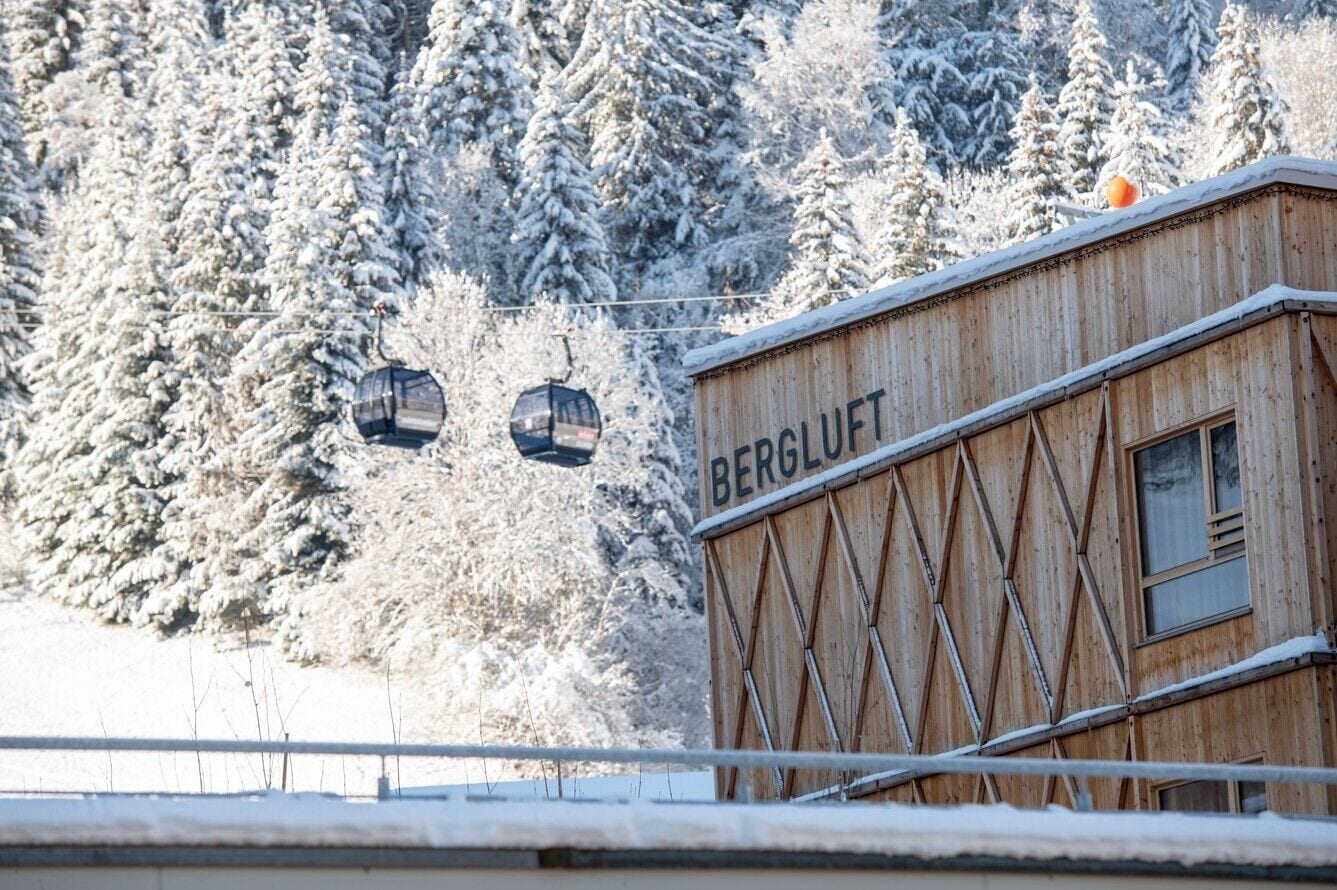 A wooden building with the word 'BERGLUFT' on its side, surrounded by snow-covered trees.