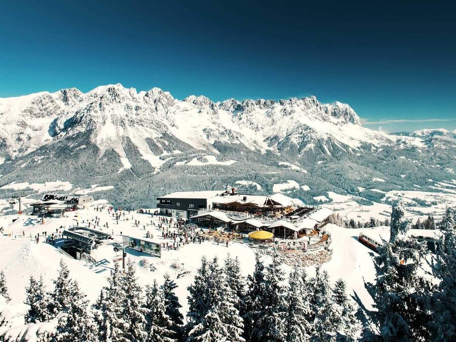 Un centro turístico invernal con montañas nevadas, pistas de esquí, un refugio y un restaurante.