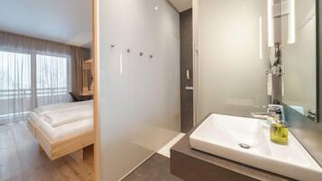 Una habitación de hotel moderna con una cama, ducha, lavamanos y un espejo grande.