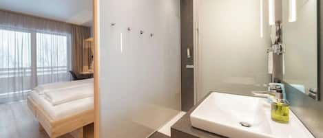 Une chambre d’hôtel moderne équipée d’un lit, d’une douche, d’un lavabo et d’un grand miroir.
