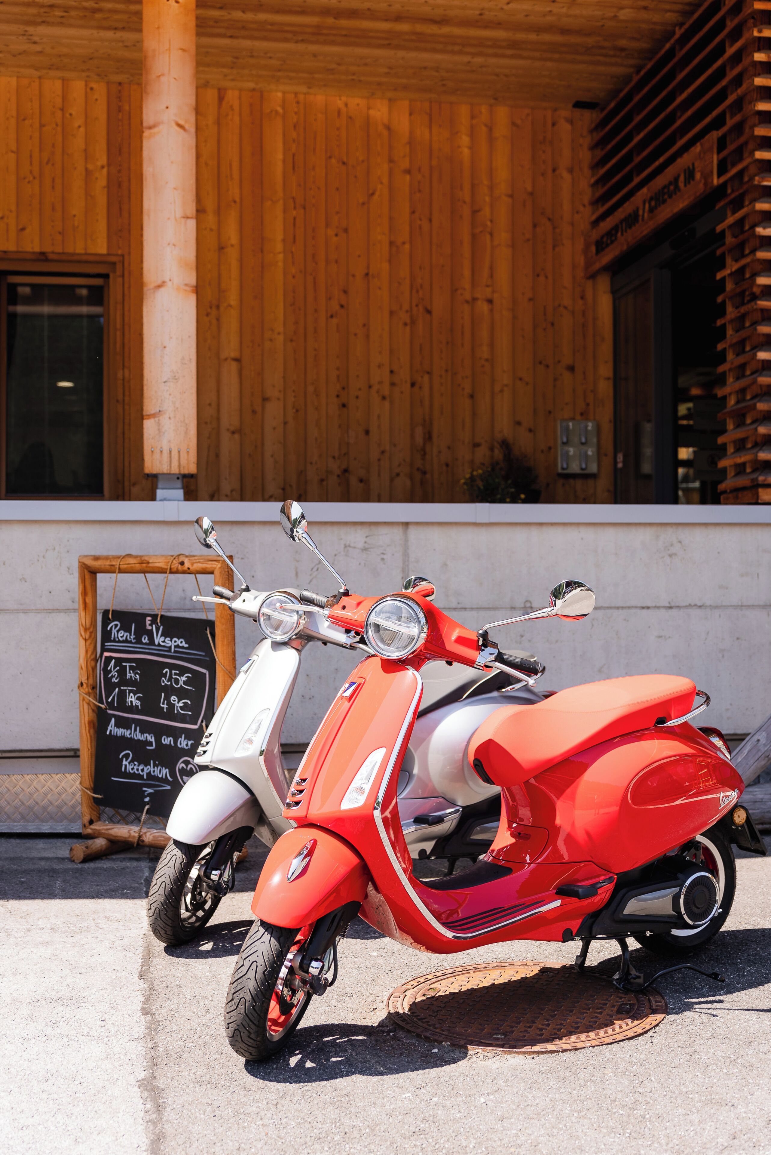 Een rode en witte scooter geparkeerd voor een gebouw met houten wanden en een prikbord.'
