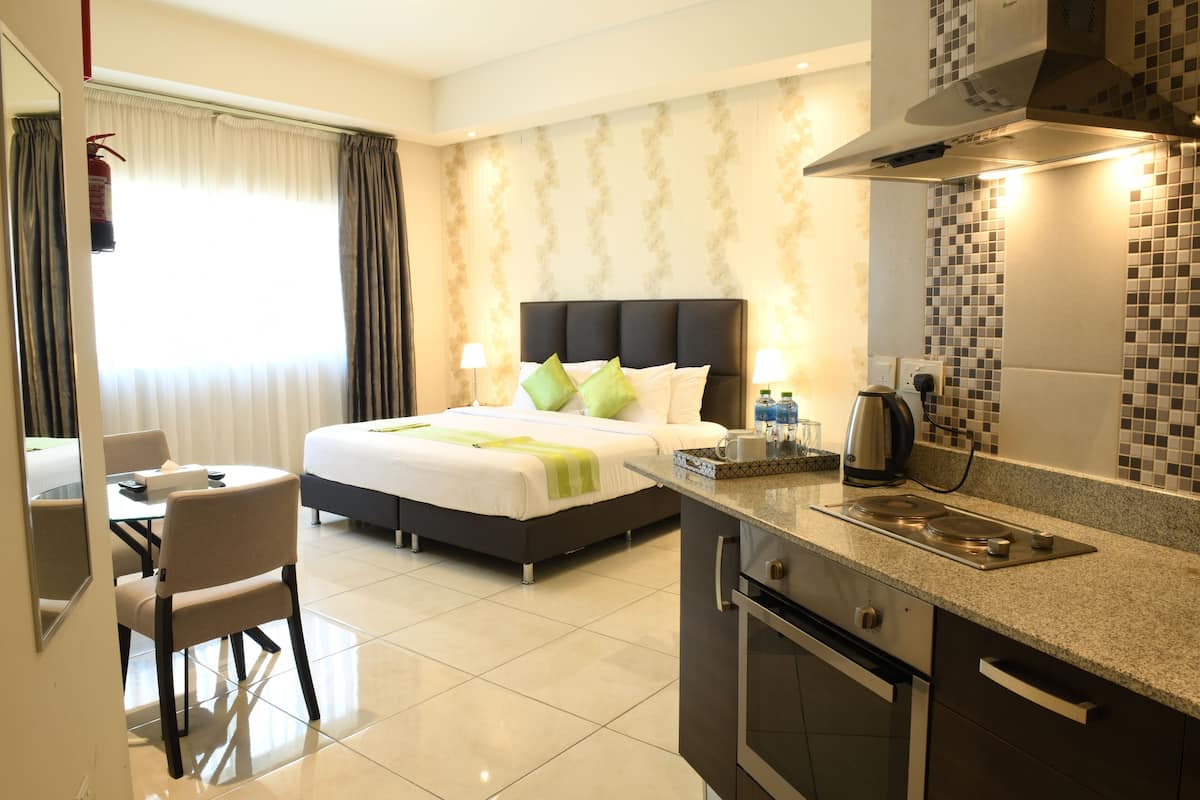 A hotel room with a bed, bedside table, lamp, and a kitchenette with a stove and sink.