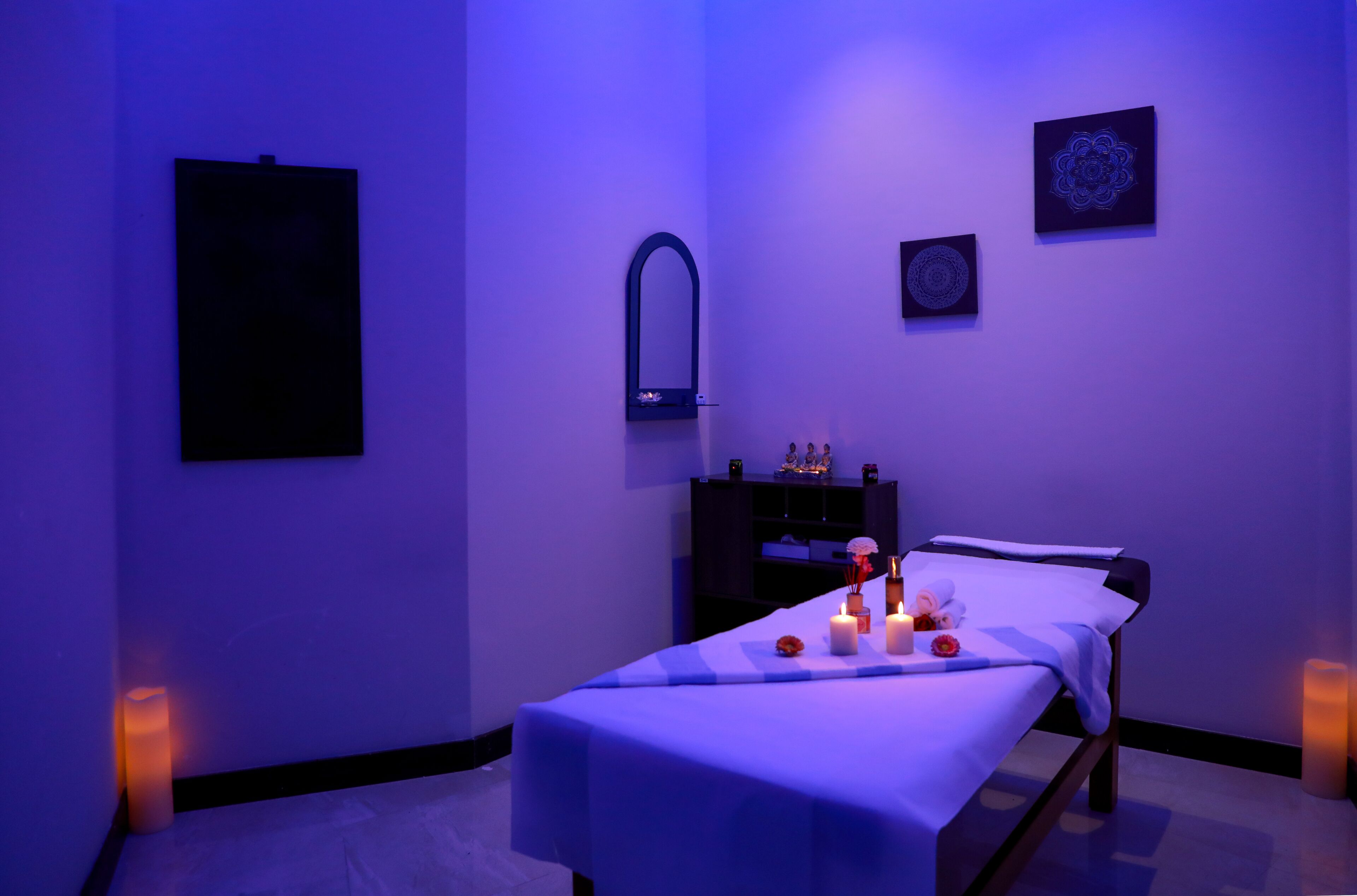 A massage room with a bed, candles, and wall art.