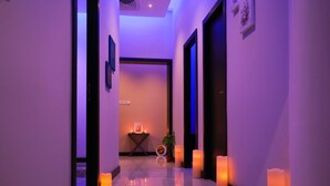 A hallway with a reflective floor, framed artwork on the walls, and candles along the sides. - Loumage S Suites and Spa (Manama)