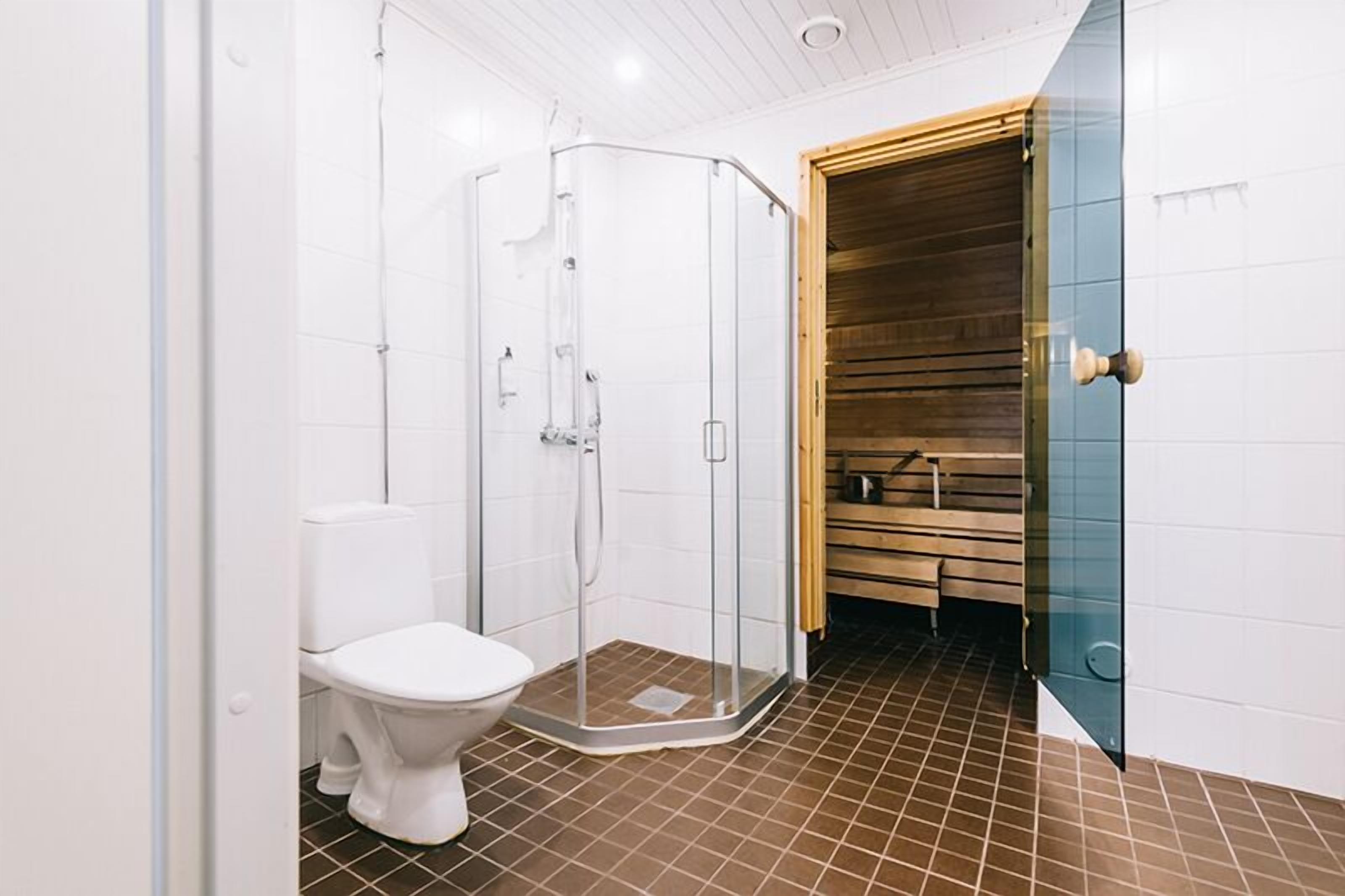 A modern bathroom with a glass shower enclosure, a white toilet, and a wooden bench.