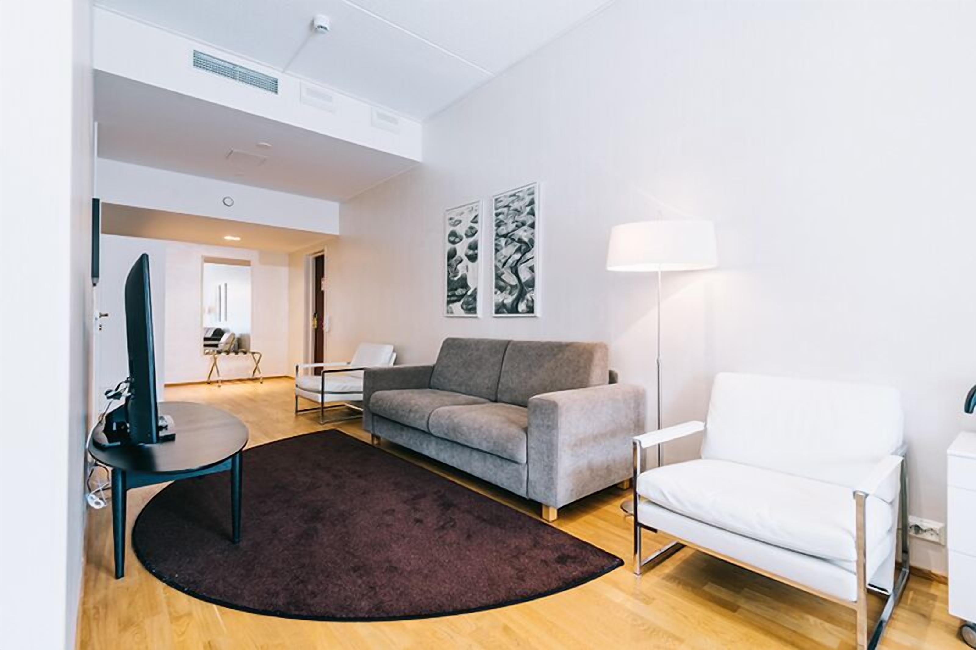 Una sala de estar moderna con un sofá gris, un sillón blanco, un tapete oscuro y una lámpara de pie.