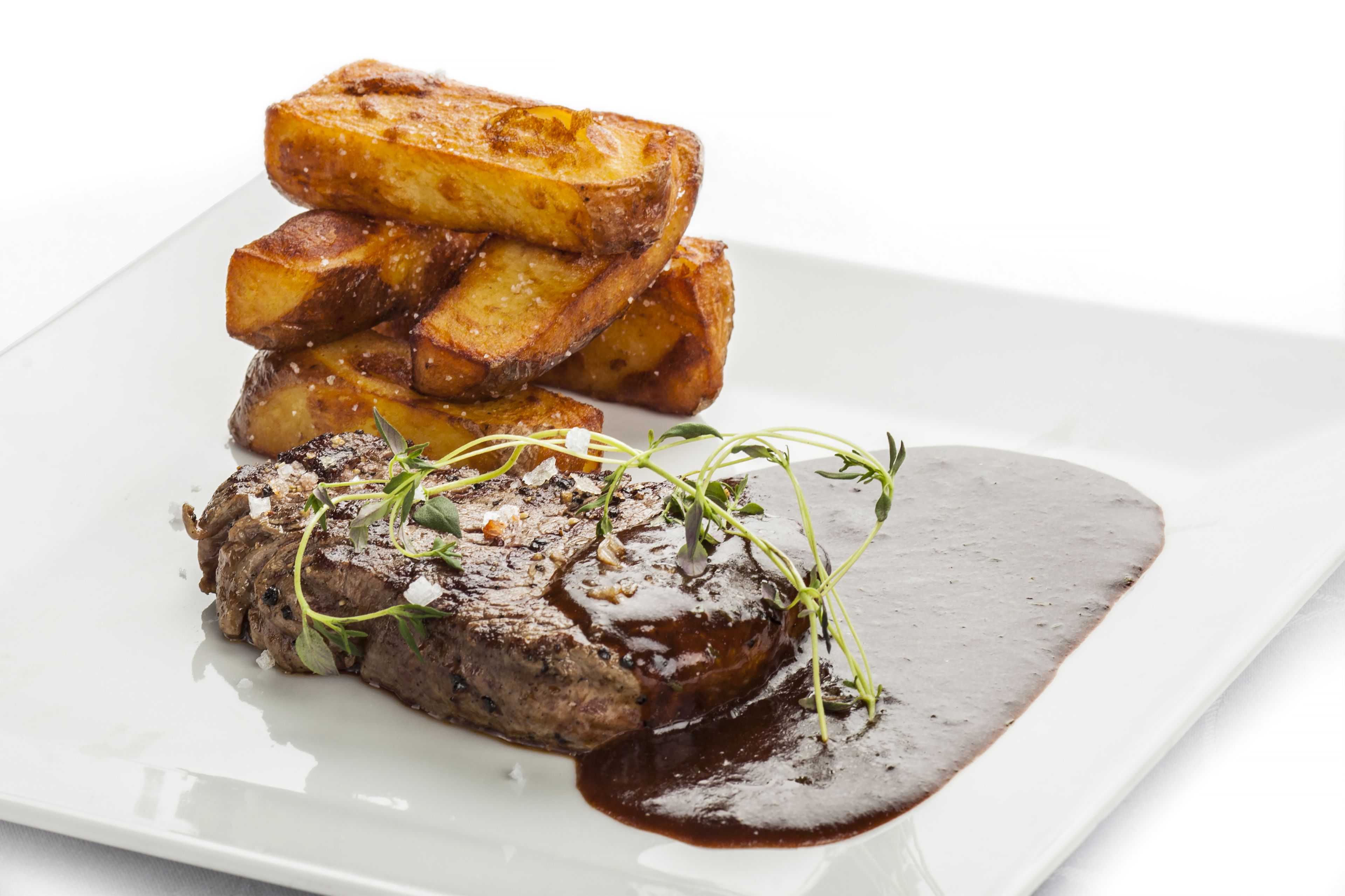 A steak with roasted potatoes and a dark sauce on a white plate.