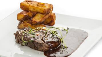 A steak with roasted potatoes and a dark sauce on a white plate.