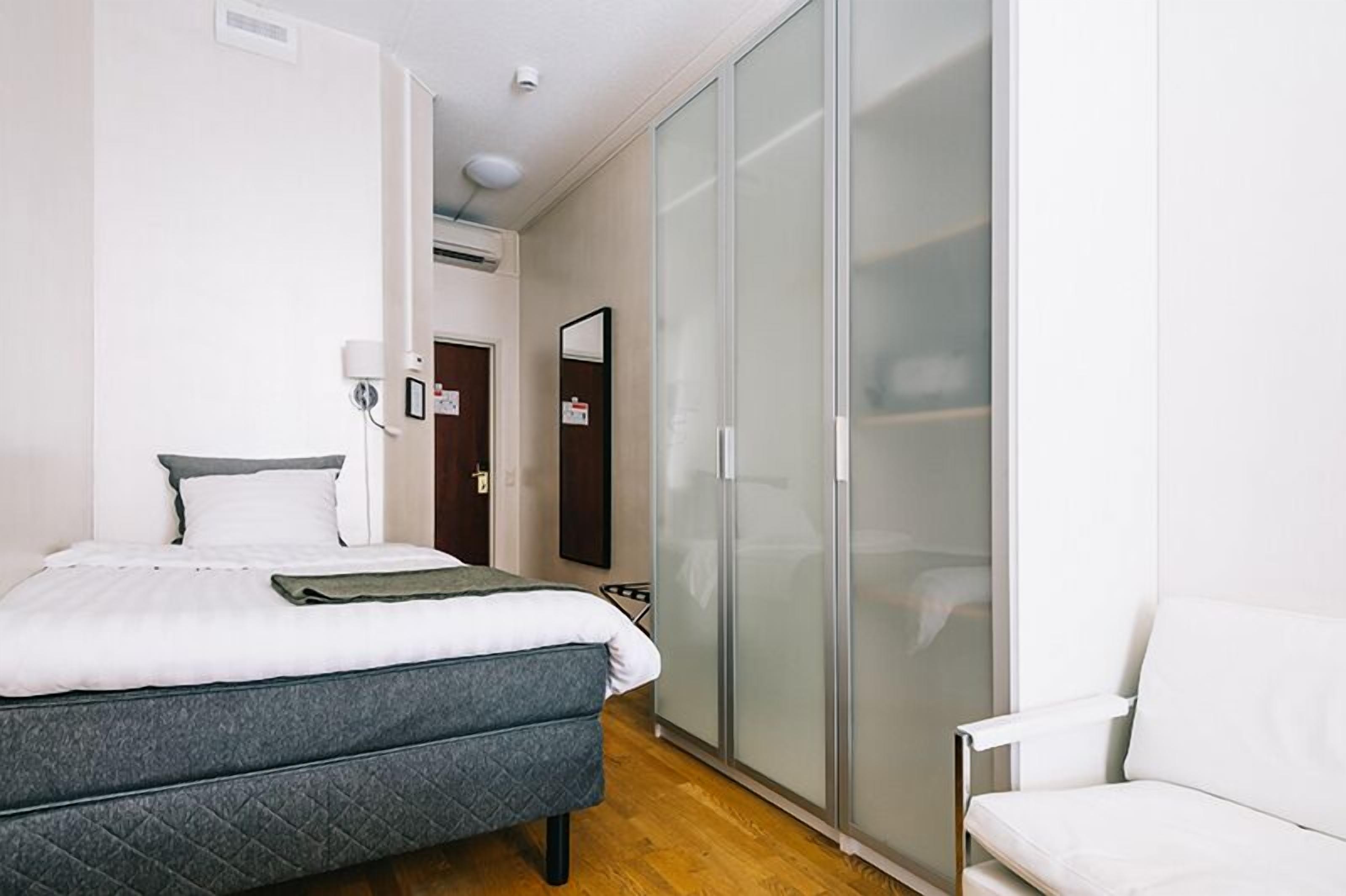 Een slaapkamer met een bed, een witte stoel, een kledingkast en een spiegel.