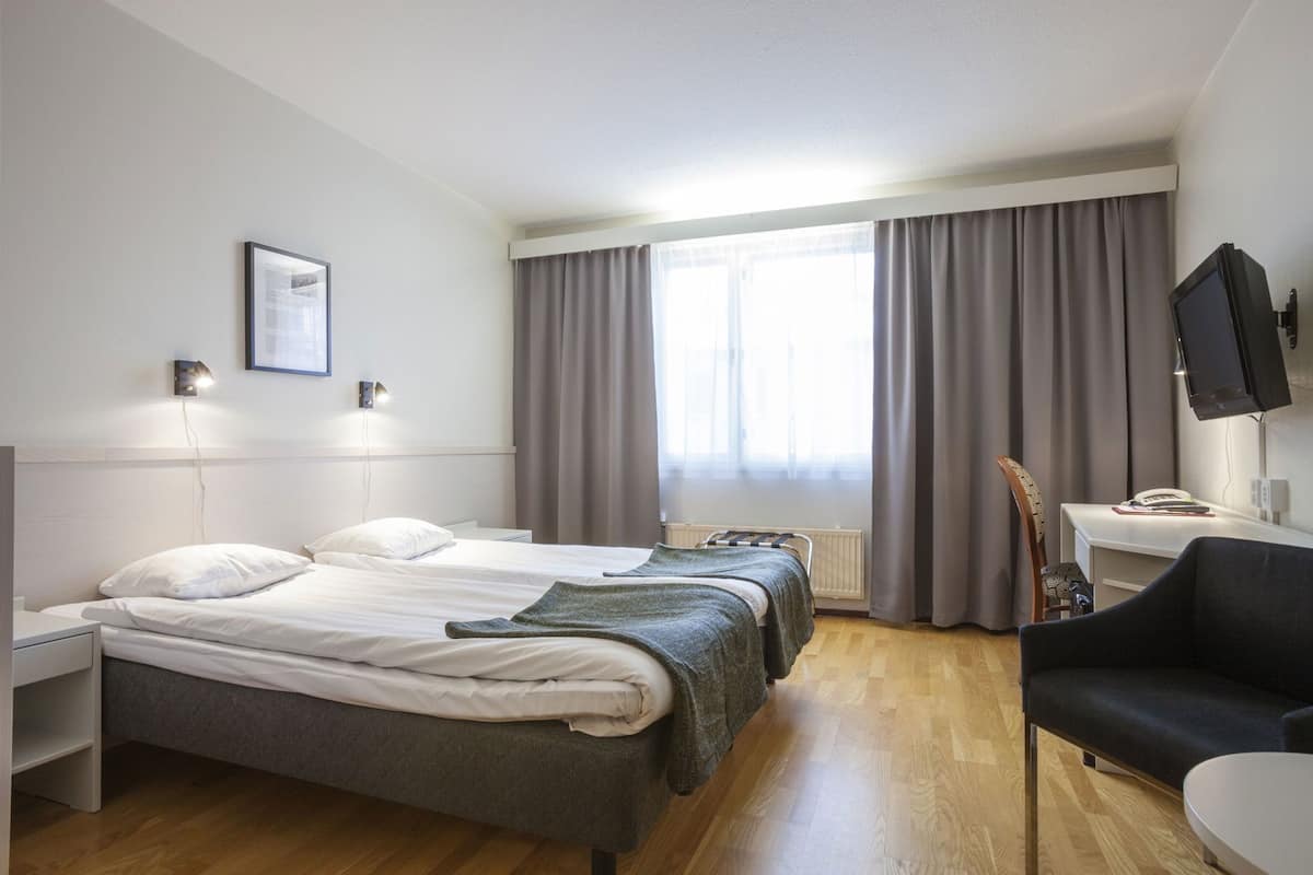 Ein Hotelzimmer mit Bett, Nachttischen, einem Schreibtisch mit Stuhl, einem Fernseher und einem Fenster mit Vorhängen.