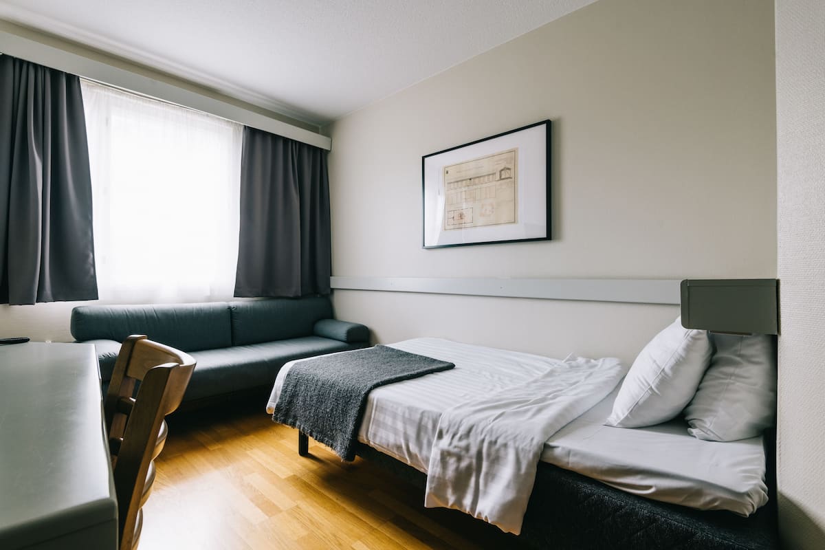 Ein modernes Hotelzimmer mit Bett, einer Couch, einem Schreibtisch und einem fensterbepflanzten Fenster.