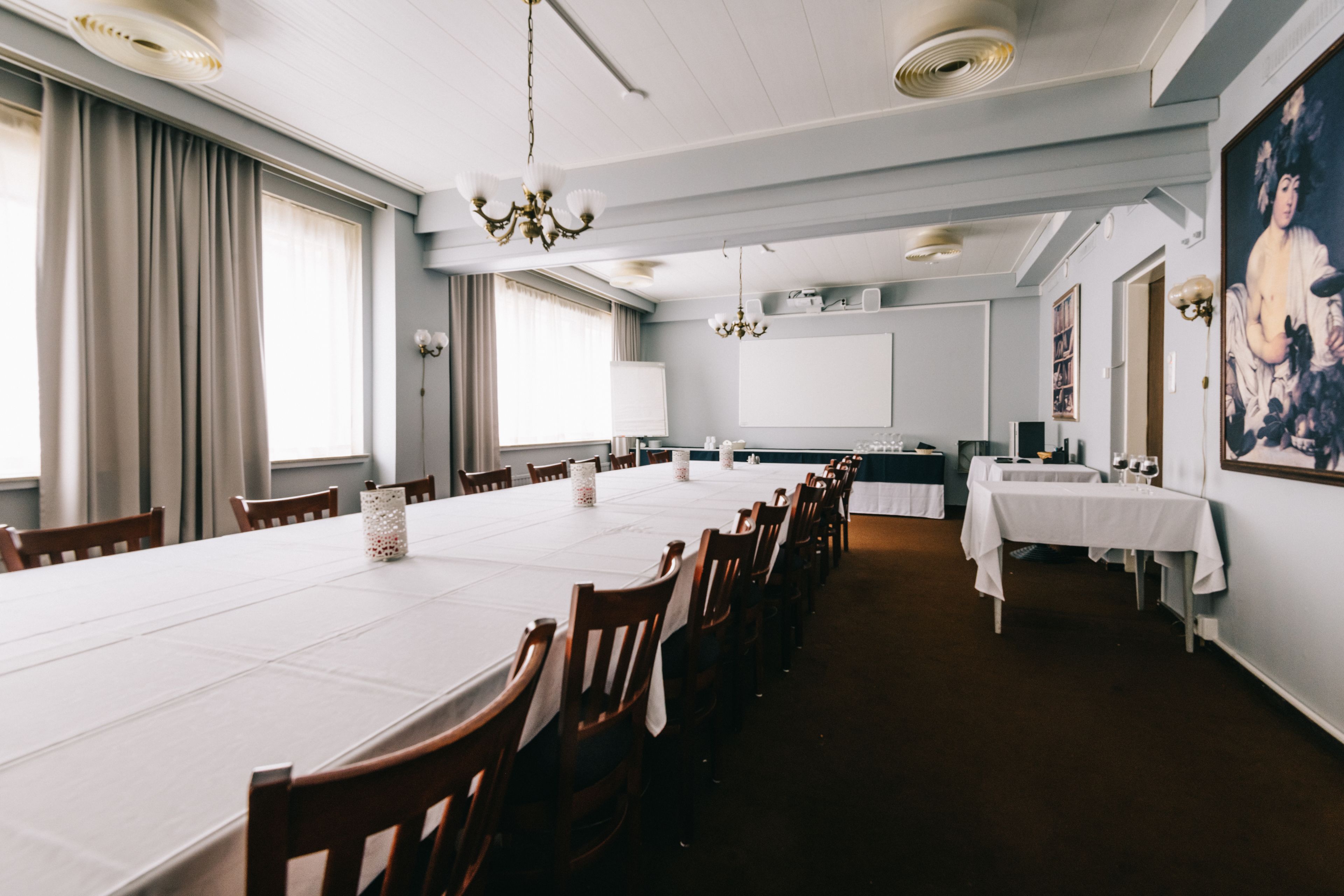 A conference room with a long table, chairs, a chandelier, and a painting on the wall.