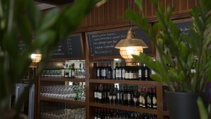 A bar area with shelves of wine bottles and glasses, a chalkboard menu, and a hanging light fixture.