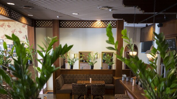 A restaurant interior with a wooden bench seating area, a round table, and potted plants.