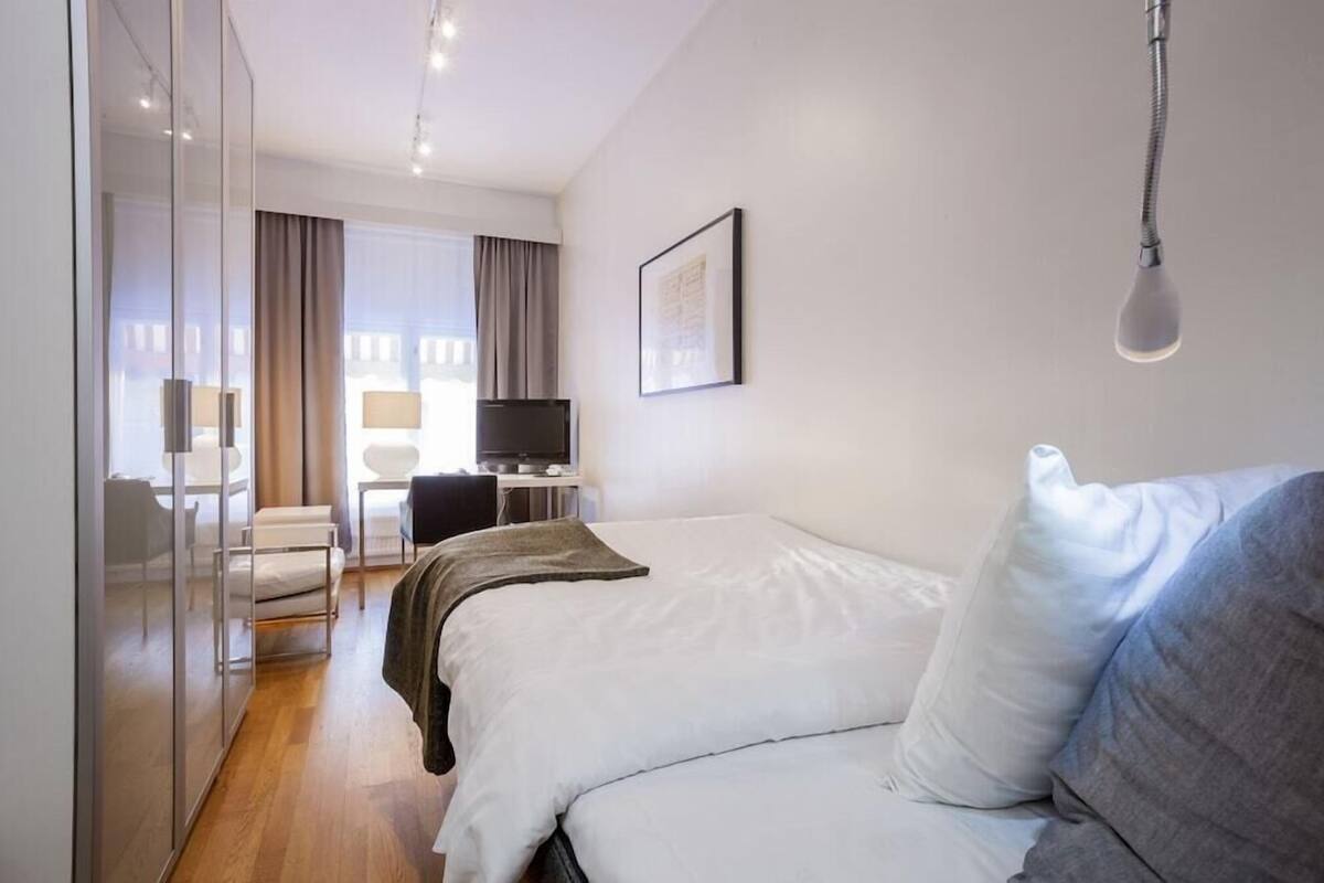 Ein Hotelzimmer mit einem Bett, einem Schreibtisch mit Computer, einem Sessel, einem Fernseher und einem Fenster mit Vorhängen.