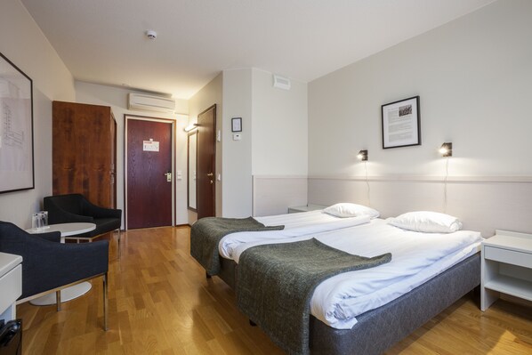 Habitación de hotel con dos camas individuales, un escritorio, una silla y un armario.