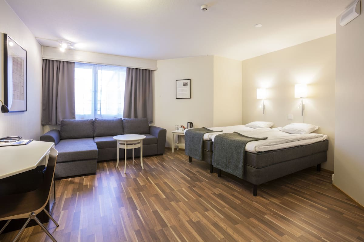 Ein modernes Hotelzimmer mit einer Couch, zwei Einzelbetten, einem kleinen Tisch und einem Schreibtisch.