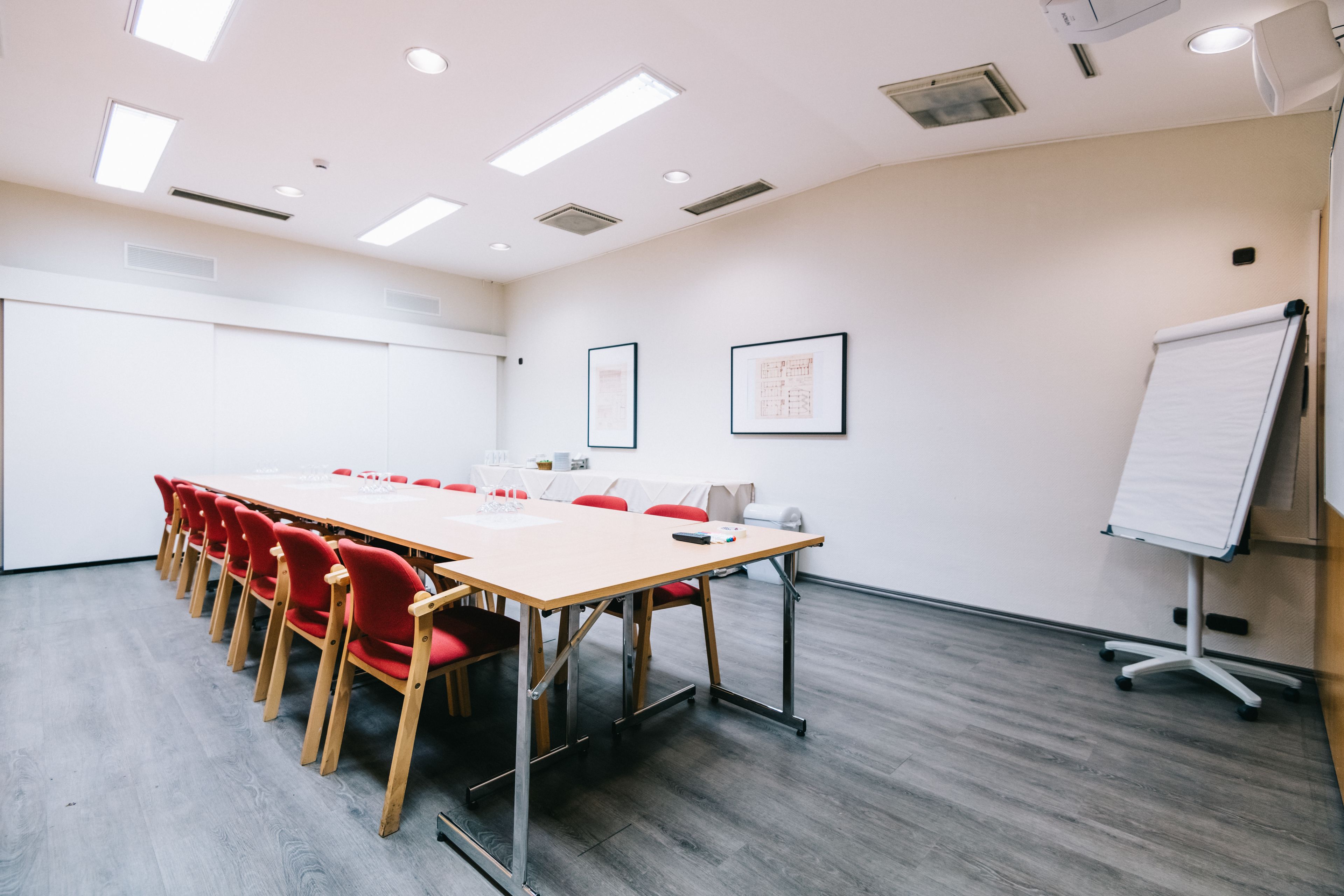 Une salle de conférence avec une longue table, des chaises rouges, un tableau blanc et des tableaux encadrés accrochés au mur.