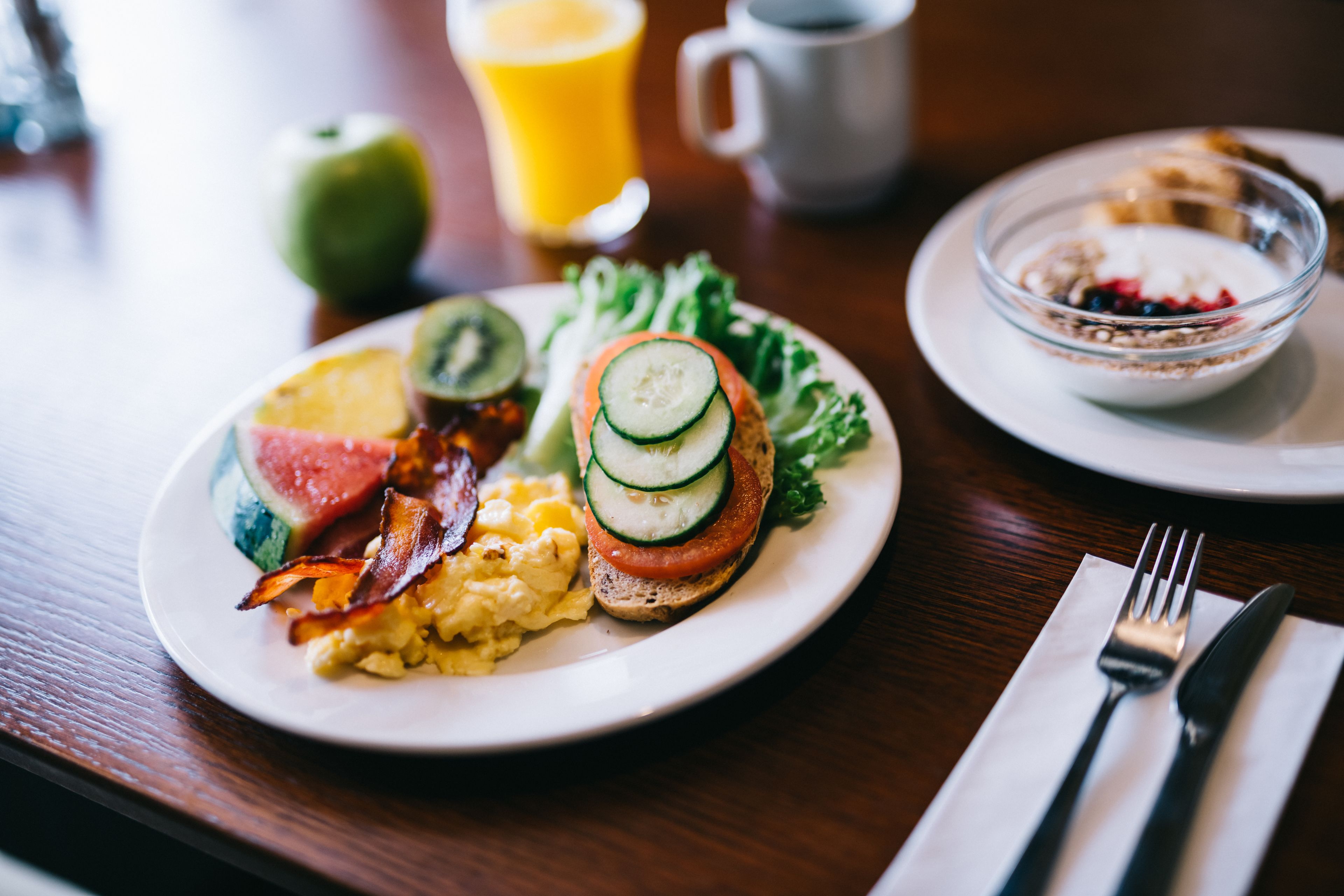 A breakfast plate with eggs, bacon, avocado, tomato, and a slice of bread, accompanied by a glass of orange juice and a coffee cup.