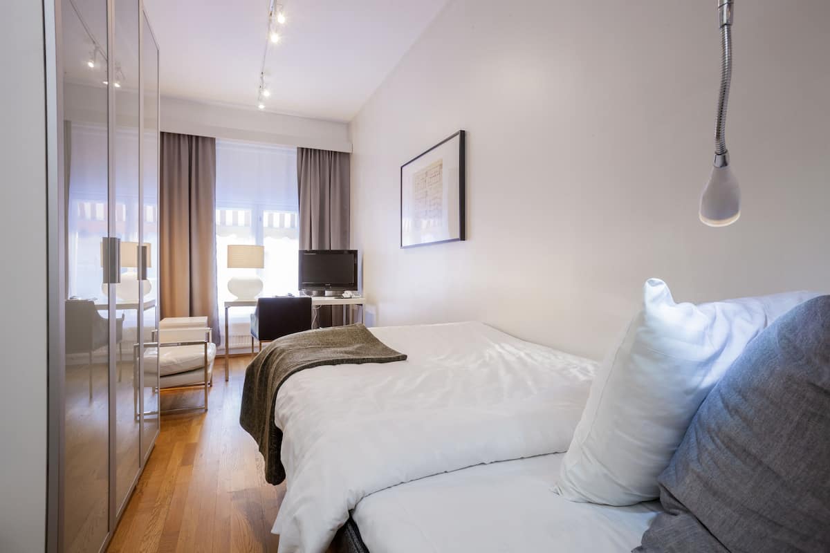Ein Hotelzimmer mit einem Bett, einem Schreibtisch, einem Stuhl, einem Fernseher und einem fenster mit Vorhängen.
