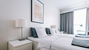A hotel room with two beds, a desk, and a window with curtains.