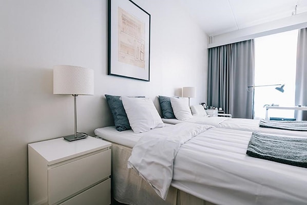 Habitación de hotel con dos camas, un escritorio y una ventana con cortinas.