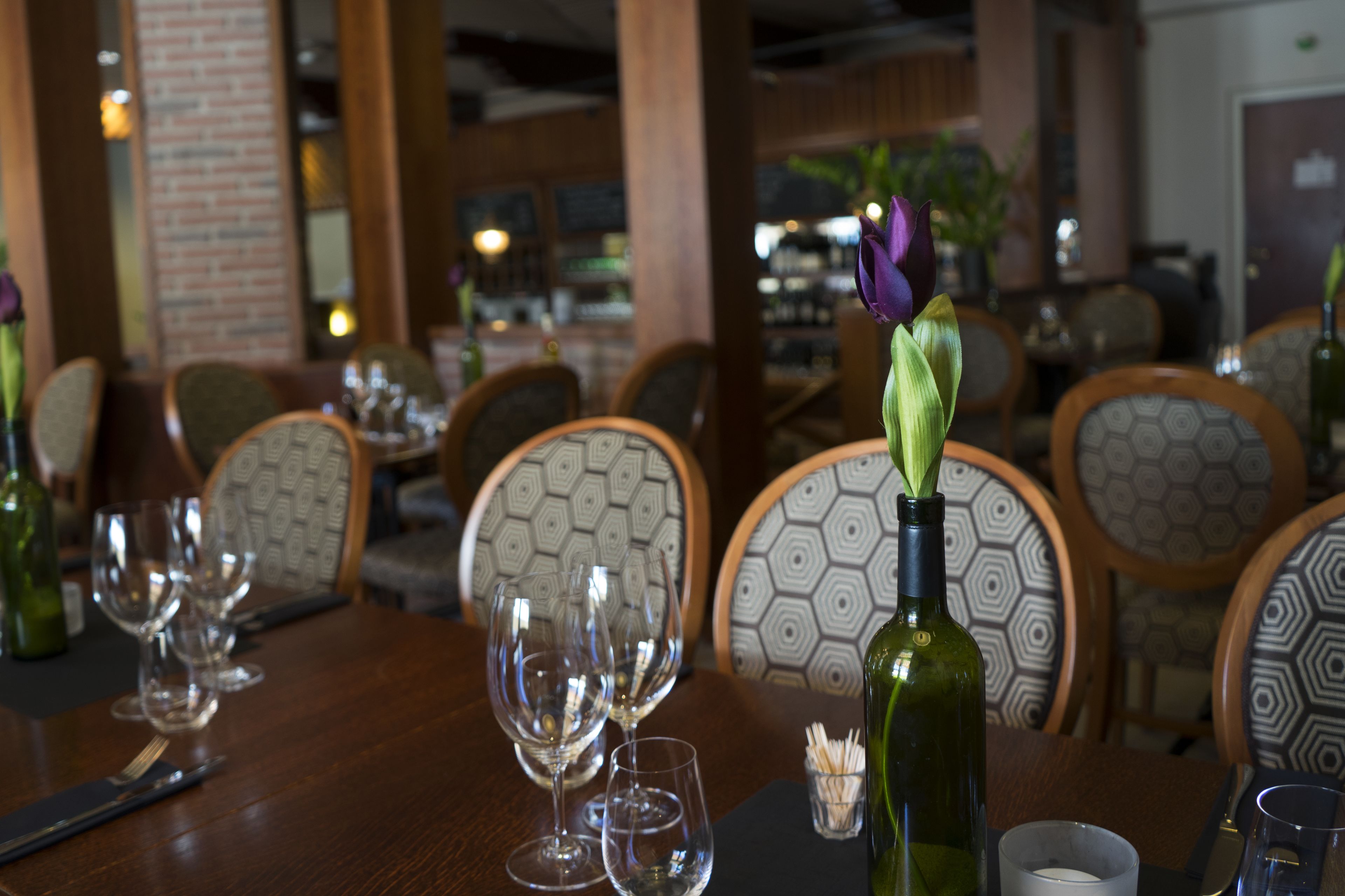 Une table en bois dressée pour un repas dans un restaurant, avec des verres à vin, une bouteille et une bougie.