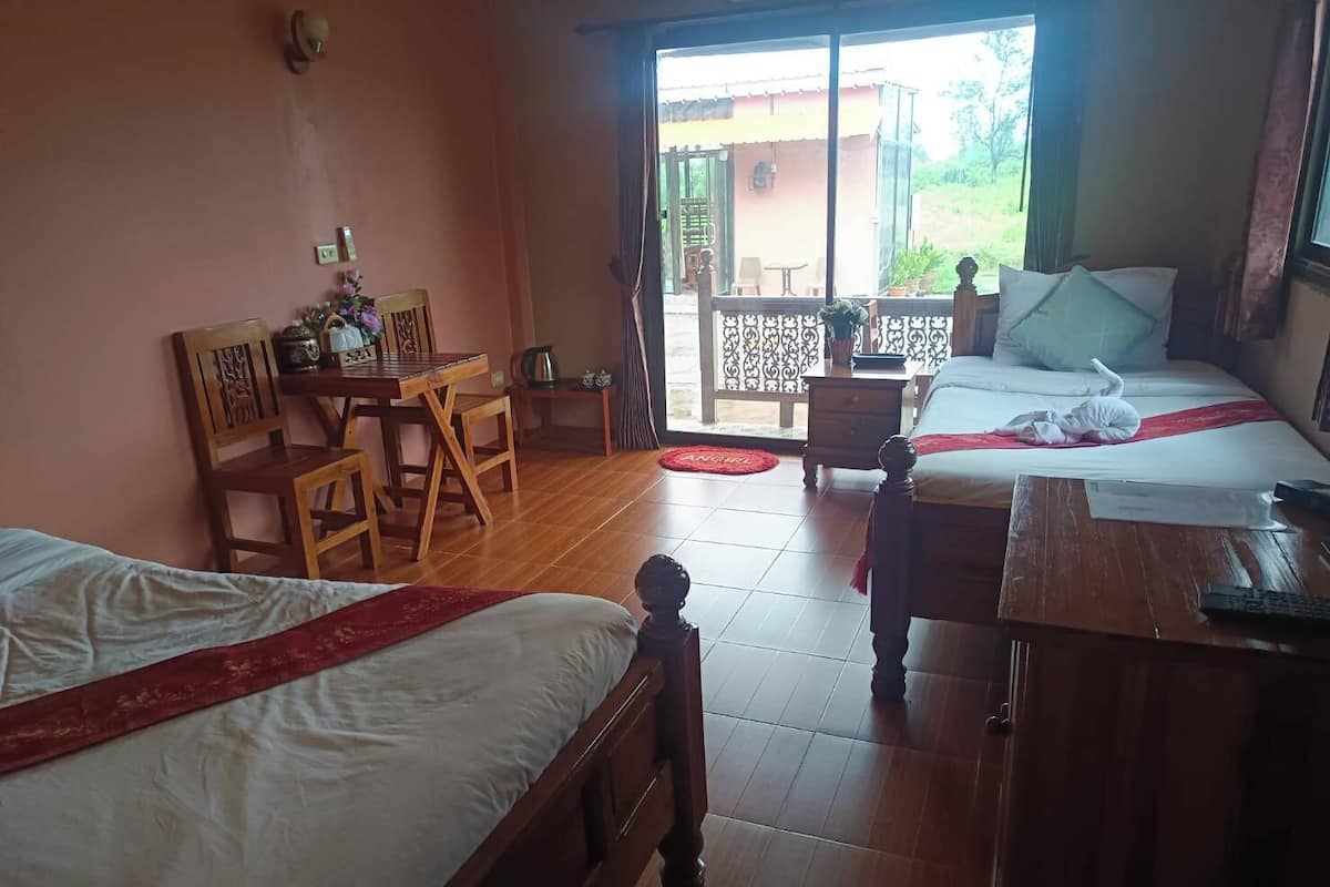 A hotel room with two beds, a dining table, chairs, a small kitchen area, and a balcony with a view.