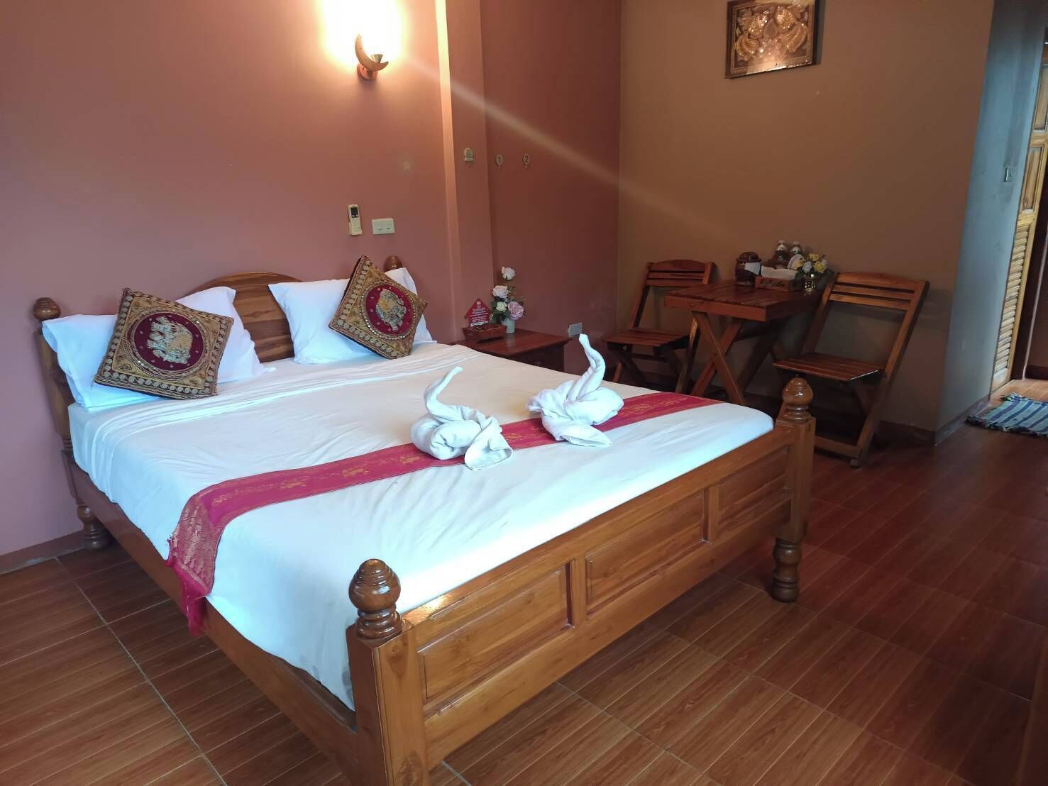 A neatly made bed with decorative pillows, a swan-shaped towel, and a wooden headboard.