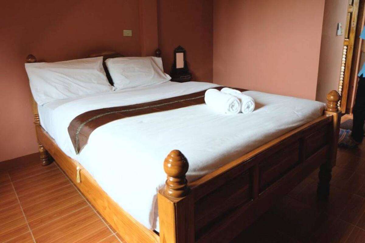 A neatly made bed with white linens and a brown bedspread, a wooden headboard, and a wooden floor.