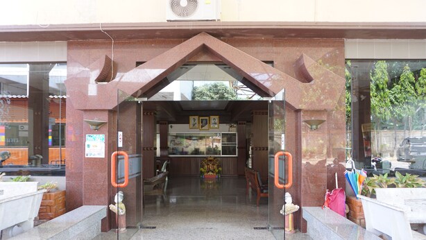 A building entrance with a glass door, a small statue, and a bench outside. - Sri Chumphon Hotel (Chumphon)