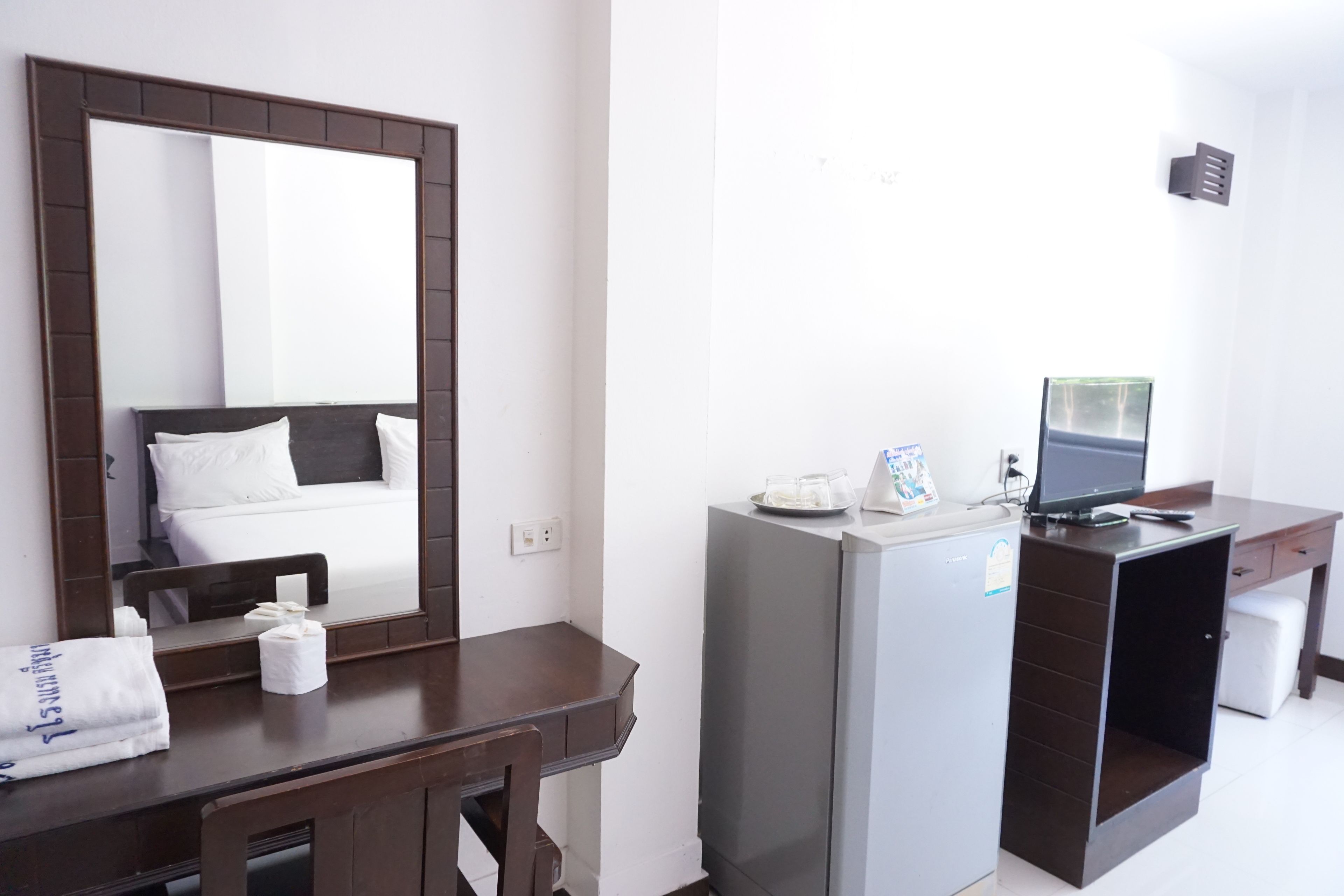 Una habitación de hotel con cama, escritorio con computadora, refrigerador y espejo.