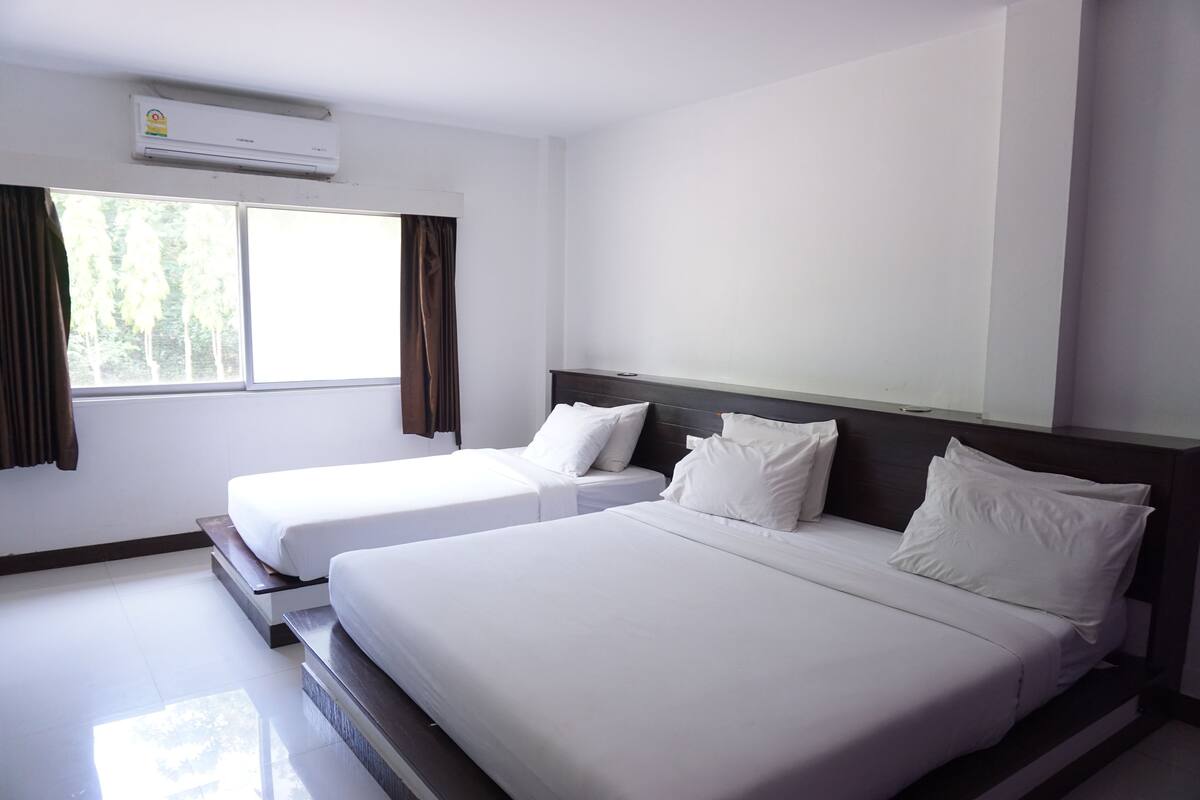 A hotel room with two single beds, a large window with curtains, and an air conditioning unit on the wall.