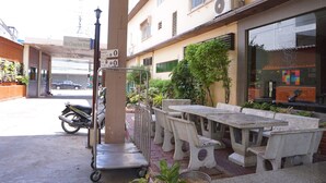An outdoor seating area with concrete tables and chairs, a motorcycle, and a street in the background. - Sri Chumphon Hotel (Chumphon)