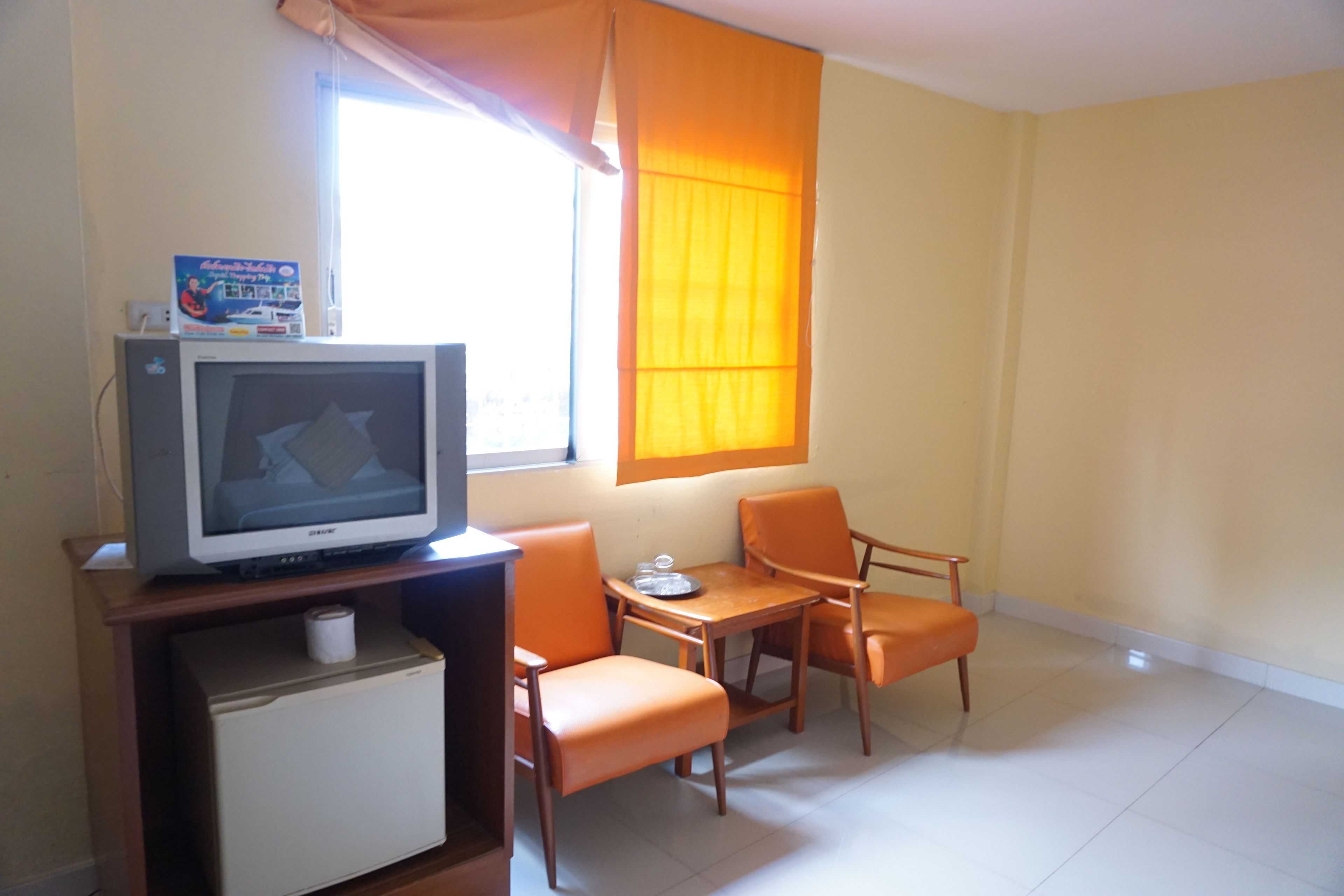 Una habitación pequeña con una televisión sobre un mueble bajo, una mesita, dos sillas y una ventana con cortinas.