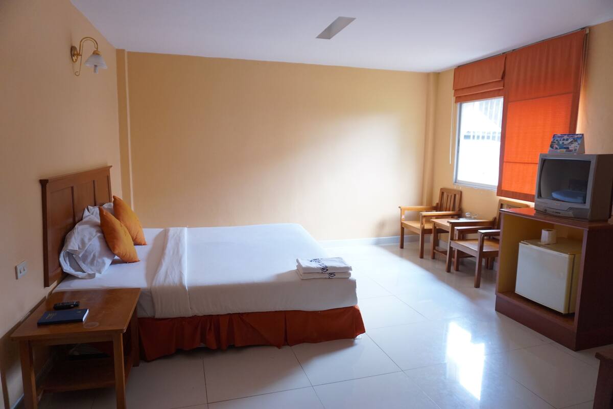 A hotel room with a bed, a desk, a chair, a television, and a window with curtains.