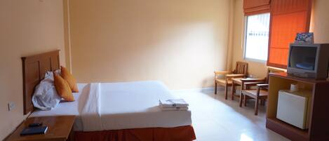 Quarto de hotel com cama, escrivaninha, cadeira, televisão e janela com cortinas.