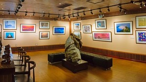 Una galería de arte con diversas obras enmarcadas en las paredes, pisos de madera y bancos para sentarse.