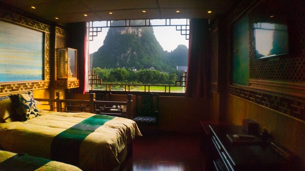 A hotel room with a large bed, a desk, and a window offering a view of a mountain. - Yangshuo Li River Gallery Lodge (Guilin)