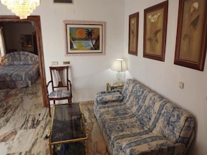 Uma sala de estar com um sofá, uma cadeira, uma mesa de centro de vidro e um quadro na parede.