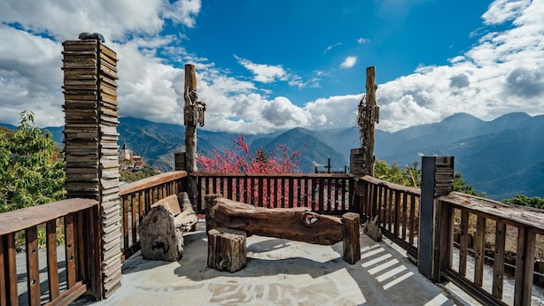 A wooden deck with a stone floor, surrounded by a wooden railing, overlooking a mountainous landscape with a clear sky. - Yunnan Homestay (Ren'ai)