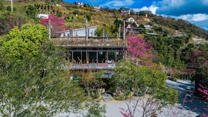 A modern building with large windows and a balcony, surrounded by lush greenery and hills in the background. - Yunnan Homestay (Ren'ai)