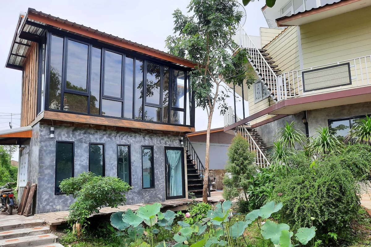 A modern two-story house with large windows, a wooden deck, and a staircase leading to a balcony.