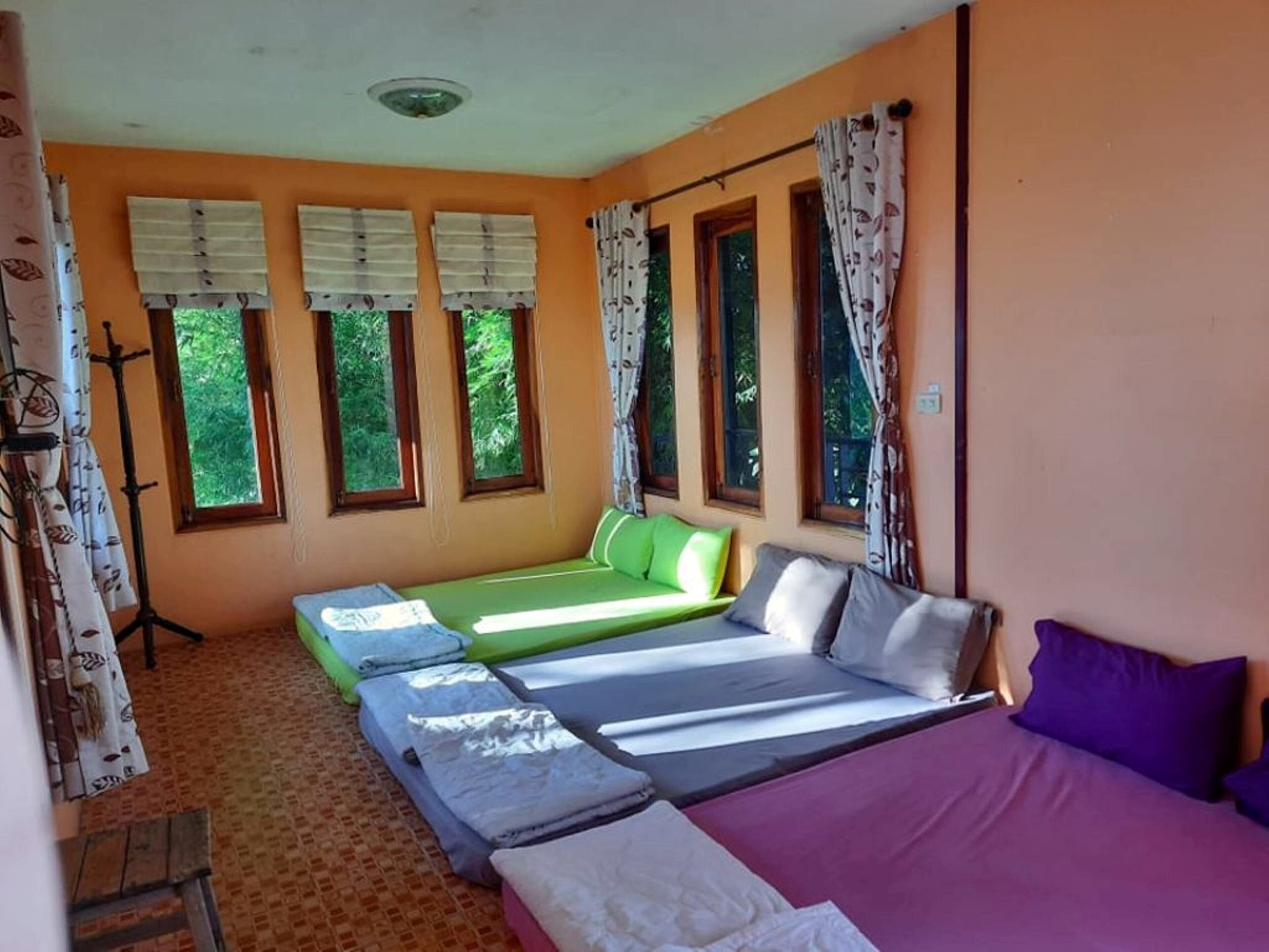 A room with two single beds and a larger bed, a small table, and a window with curtains.