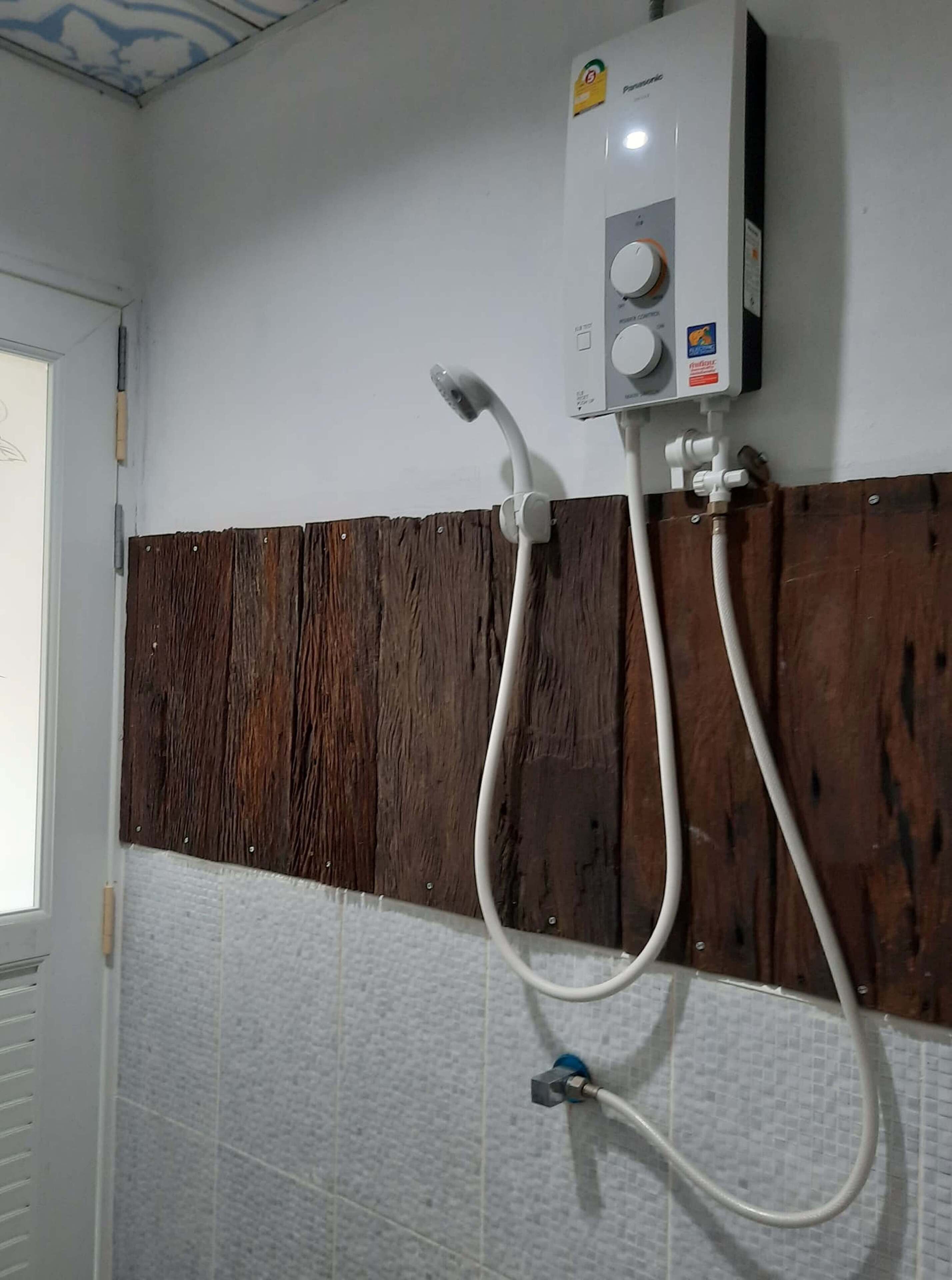 Casa de banho com chuveiro fixado na parede, painel de madeira e chão em azulejos.