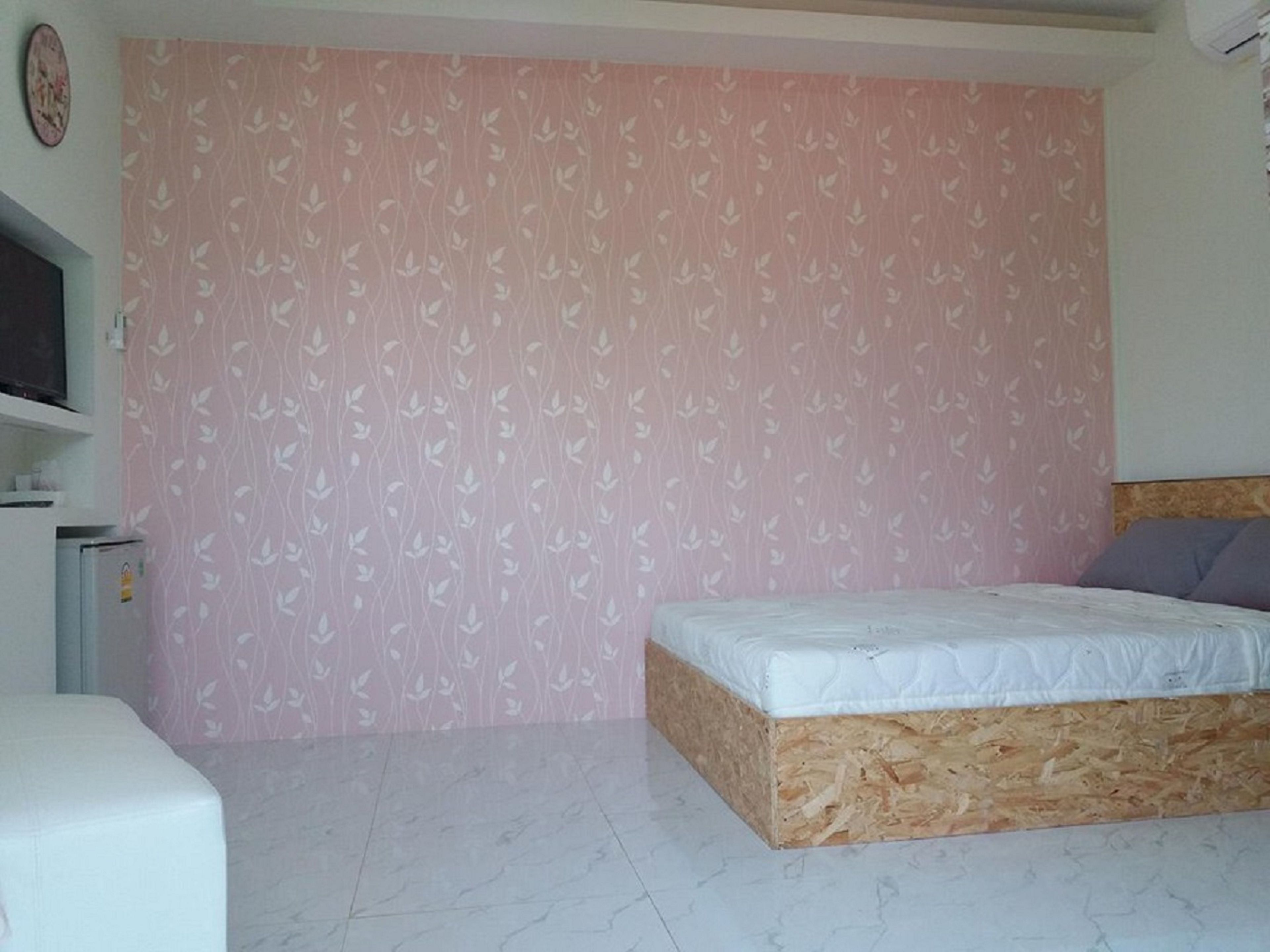A bedroom with a bed, a small white cabinet, and a pink patterned wall.