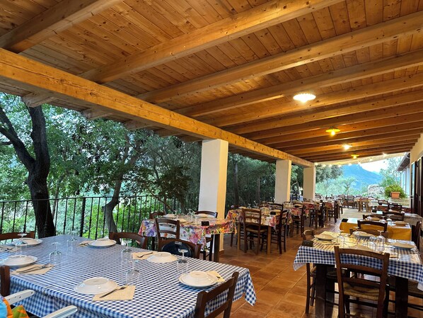 Um restaurante ao ar livre com toalhas de mesa xadrez, vigas de madeira e vista para árvores e montanhas.