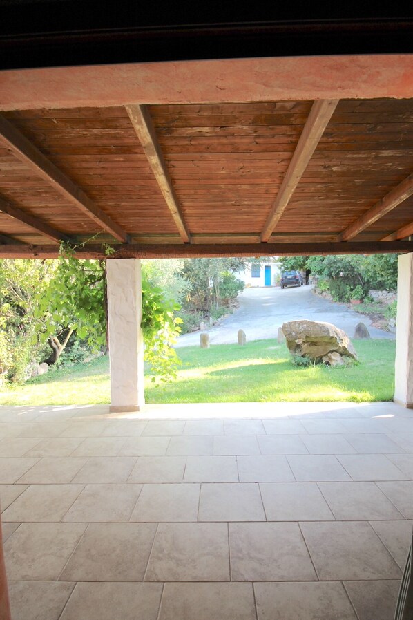 A covered patio area with a tiled floor and wooden beams. - Agriturismo Piperedda (Irgoli)