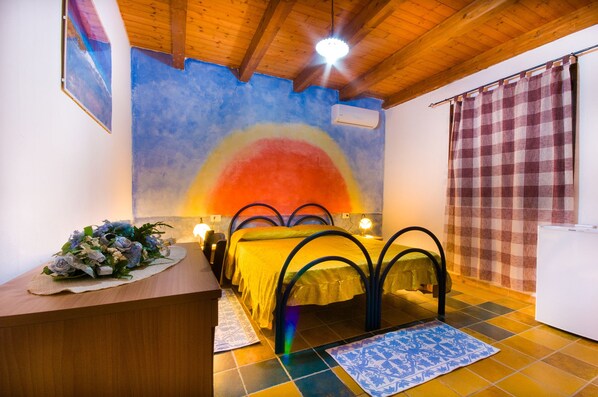 Una habitación con cama, escritorio, un mural en la pared y una cortina a cuadros.